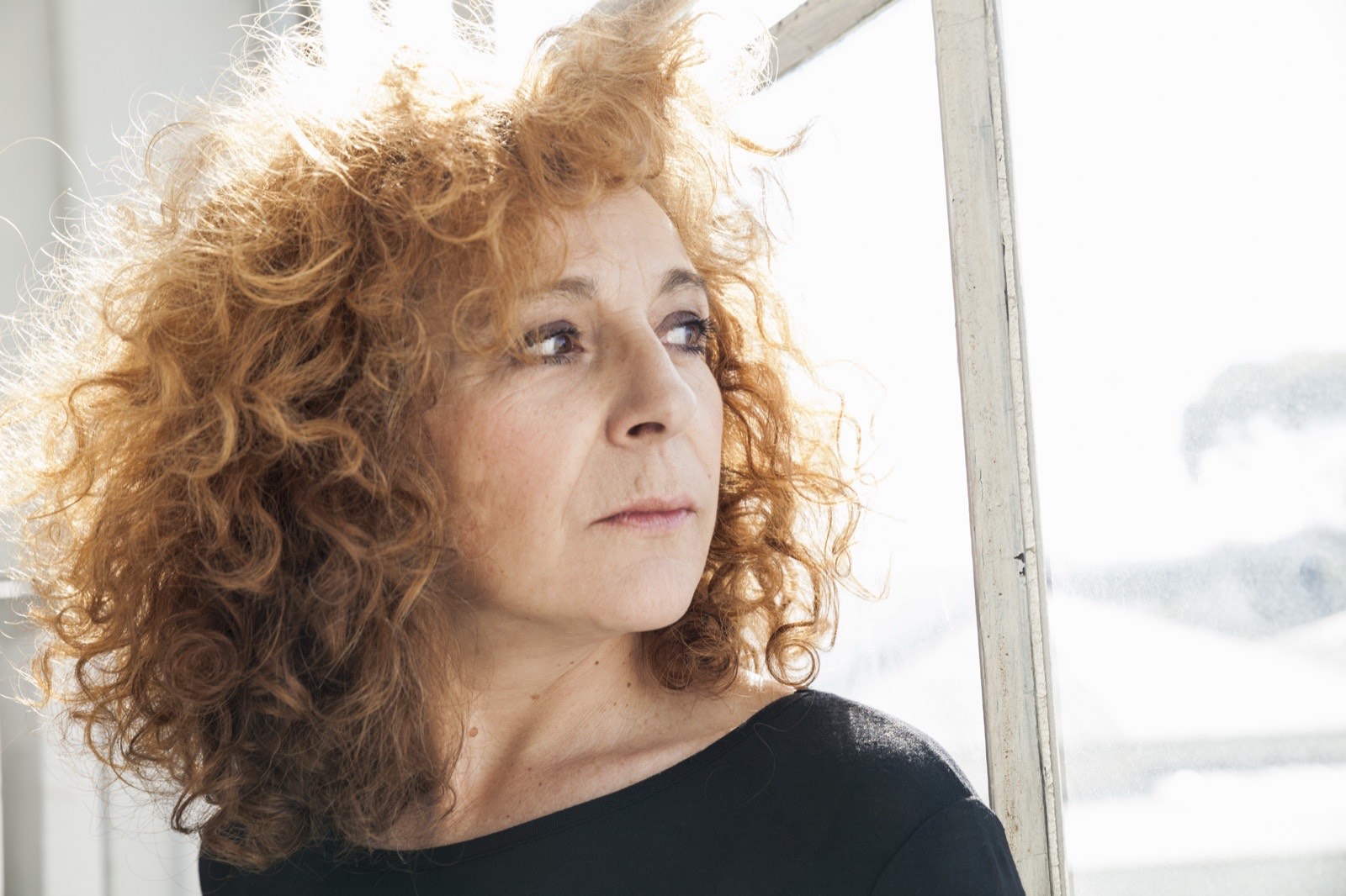A woman looking out of a window in soft daylight